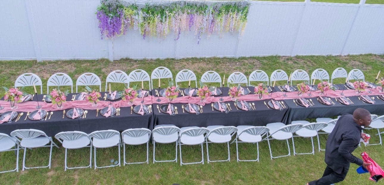 Elegant outdoor long-table setup with white chairs and floral décor